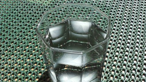 Ein klarer Glas mit Wasser steht auf einer strukturierten Oberfläche aus grünem Material und reflektiert Licht.