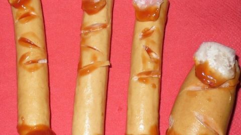 Auf einem roten Tisch liegt ein Buffet mit gruselig gestalteten Würstchen, die wie abgetrennte Finger aussehen.