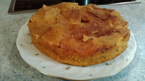 Ein glutenfreier Apfel-Mandelkuchen ruht auf einem weißen Teller, umgeben von einer hellen Küchentheke.