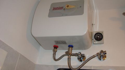 Ein kleiner Warmwasserbereiter hängt an einer Wand und versorgt effizient einen Badezimmerbereich mitWarmwasser.