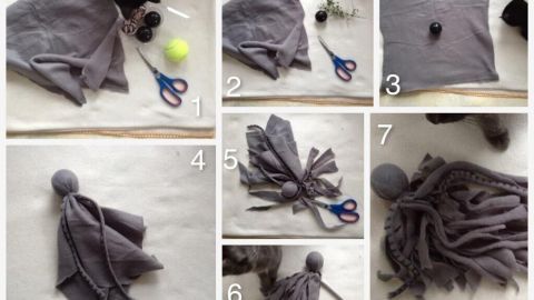 Graues Katzenspielzeug wird aus Stoff und anderen Materialien gestaltet, während eine Hand dabei die Schere hält.
