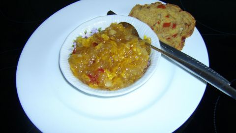 Ein Schälchen Kürbis-Chutney steht auf einem weißen Teller, daneben liegt ein Stück Brot. Chutney wird serviert.