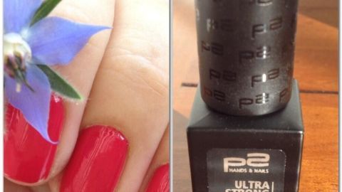 Ein Nagelhärter von P2 wird auf einem Tisch präsentiert, während eine Hand mit rot lackierten Nägeln und einer Blume im Hintergrund sichtbar ist.