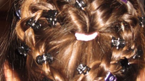 Ein Haarstylingsobjekt mit Zöpfen und bunten Haargummis wird in einem häuslichen Umfeld präsentiert.