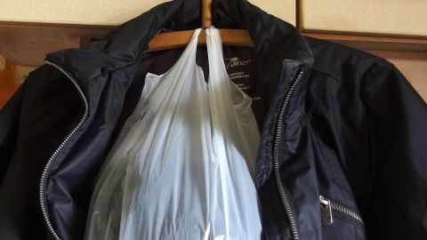 Eine Jacke hängt an einem Kleiderhaken, während eine durchsichtige Tüte mit einem Schal, Handschuhen und einer Mütze darin befestigt ist.
