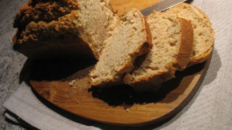 Wattekuchen-Scheiben liegen frisch geschnitten auf einem Holzbrett neben einem Messer auf einem dunklen Küchentisch.