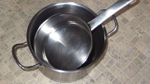 Ein Edelstahltopf mit einem Löffel liegt nebeneinander auf einer neutralen Küchenoberfläche, bereit zum Kochen.