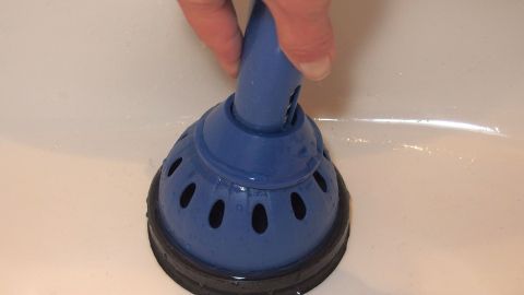 Ein Handwerker benutzt einen blauen Pümpel, um einen verstopften Abfluss in einem Waschbecken zu reinigen.