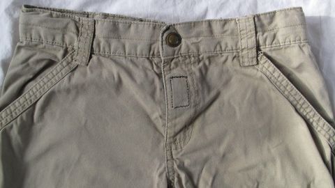 Beige Kinderhose mit defektem Reißverschluss auf einem weißen Untergrund, bereit zum Ersetzen durch Klettband.