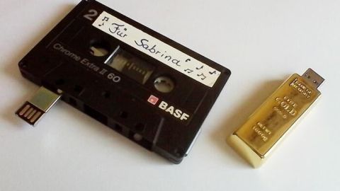 Ein alter Kassettenträger und ein paralleler USB-Stick, der kreativ gestaltet ist, stehen auf einem neutralen Hintergrund.