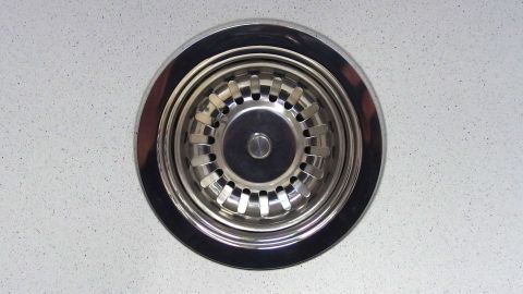 Ein Abfluss mit einem silbernen Sieb in einer modernen Küchenarbeitsplatte, bereit für die Reinigung mit Spülmaschinenpulver.