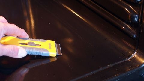 Ein Handwerker entfernt mit einem Schaber starke Verkrustungen von der glatten Oberfläche eines Backofens.