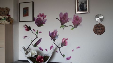 An einer Wand im Schlafzimmer schmücken zarte Magnolien-Wandtattoos den Raum, während eine elegante Vase mit Blumen auf einem Regal steht.