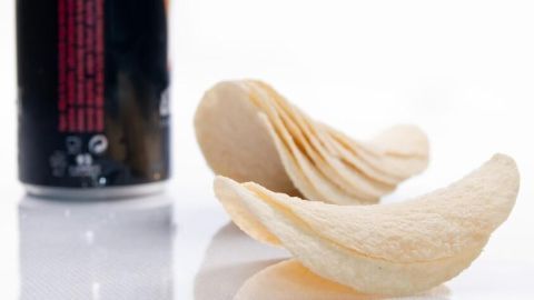 Chips liegen vor einer Getränkedose auf einer weißen Oberfläche. Die Szene zeigt typische Light-Produkte im Alltag.