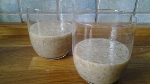 Zwei Gläser mit einem cremigen Apfel-Kokos-Smoothie stehen auf einer Holzfläche vor einer hellen Fliesenwand.