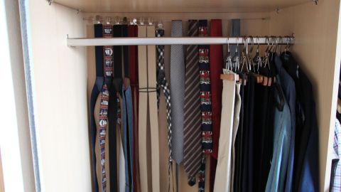 Ein Kleiderschrank ist gut organisiert, mit einem Regal oben und einer Stange für Gürtel und Hosen darunter, alles ordentlich verstaut.