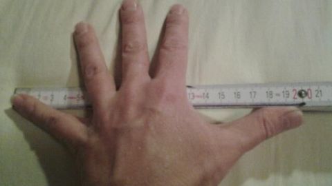 Eine Hand liegt auf einem Zollstock, der misst, während der Hintergrund eine helle Oberfläche zeigt.