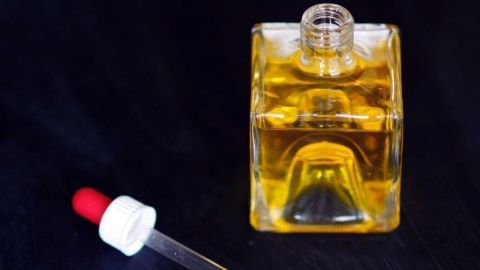 Ein Fläschchen mit Mandelöl steht neben einer Pipette auf einem dunklen Untergrund, bereit zur Anwendung gegen Ohrenschmerzen.