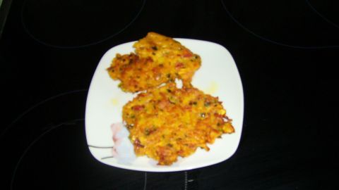 Kürbisrösti liegt auf einem Teller und wird auf einer dunklen, glatten Kochplatte präsentiert.