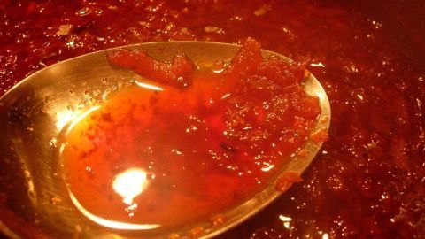 Eine silberne Löffel mit weinroter Quittenmarmelade glänzt in einem warmen, tiefen Topf, während sie optimal eingekocht wird.