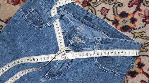 Eine Jeans liegt auf einem dekorativen Teppich, umgeben von einem Maßband, das die Maße für das Abnehmen anzeigt.
