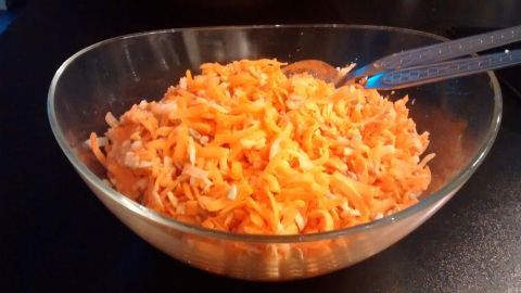 Eine Schüssel mit frisch geriebenem Möhrensalat steht auf einem Tisch, umgeben von Utensilien zum Servieren.