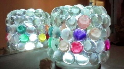 Zwei dekorative Leuchtgläser aus Glas mit bunten Kappen strahlen sanftes Licht aus und schmücken eine gemütliche Umgebung.