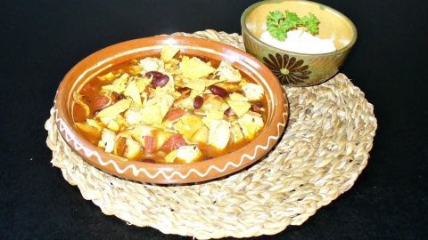 Eine scharfe H&auml;hnchensuppe in einer dekorativen Sch&uuml;ssel, serviert auf einer rustikalen Unterlage mit einer kleinen Schale.