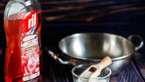 Eine Flasche Geschirrspülmittel steht neben einer Schüssel mit Zucker, während eine Pfanne auf einem Holztisch platziert ist.