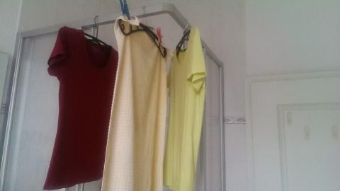 Bunte Shirts hängen an Kleiderbügeln in einem hellen Raum und trocknen ohne Wäscheleine während des Urlaubs.