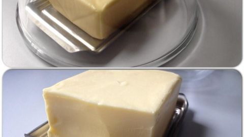 Ein Block Butter liegt auf einem Teller, während ein Messer gerade eine Portion abnimmt, um ihn streichfähig zu machen.