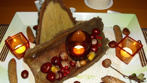 Eine herbstliche Tischdekoration aus Naturmaterialien zeigt eine Holzscheibe in einer eleganten Anordnung mit Kerzen und Frucht.