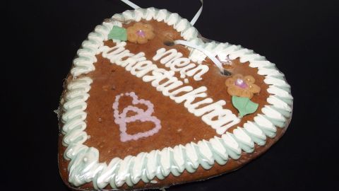 Ein Herzlebkuchen hängt von einer Schnur und trägt die Aufschrift "Mein Herz". Er ist mit Zuckerguss und Blümchen dekoriert.