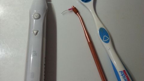 Eine elektrische Zahnbürste und zwei Hilfsmittel liegen auf einer weißen Oberfläche, bereit für die Anwendung der fluoridfreien Zahncreme.