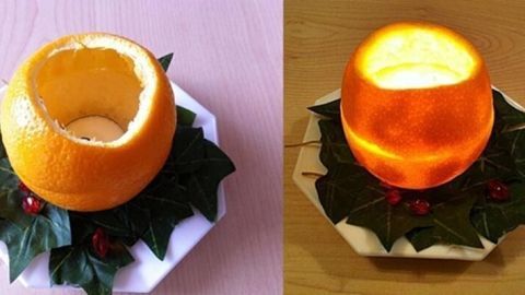 Eine ausgehohlte Orangenschale leuchtet sanft auf einem geschmückten Teller, umgeben von grünen Blättern und Deko.