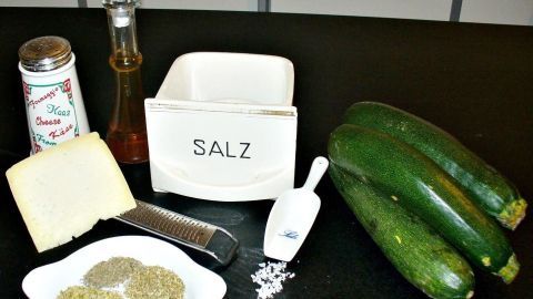Auf der Arbeitsfläche stehen frische Zucchini, Kräuter, Parmesan und Salz in einem Behälter, bereit zum Rösten.