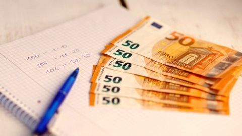 Fünf 50-Euro-Scheine liegen auf einem Notizblock, während ein Stift daneben steht. Budget erstellen, um gezielt zu sparen.