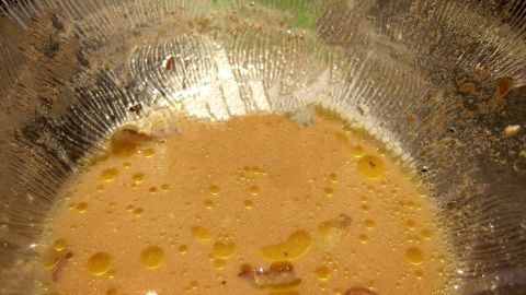 Eine transparente Schüssel mit einer geschmackvollen Salatsoße. Reste schwimmen auf der Oberfläche, umgeben von einer Küchenumgebung.