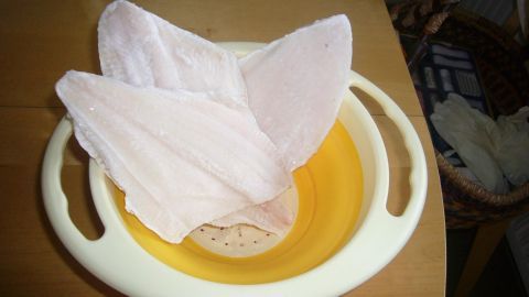 Gefrorenes Geflügel liegt in einer gelben Schüssel, während es antaut und bereit ist, weiterverarbeitet zu werden.