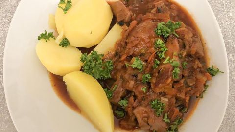 Auf dem Teller liegt ein herzhaftes Wildgulasch, das von frischen Kartoffeln und Grün dekoriert ist.