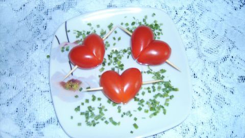 Herzförmige Tomatenstücke auf einem Teller, gehalten von Zahnstochern, dekoriert mit Schnittlauch, auf Spitze.