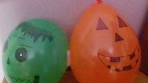 Zwei dekorative Luftballons, einer grün mit Monster-Motiv und einer orange mit Kürbis-Gesicht, schmücken eine Party-Ecke.