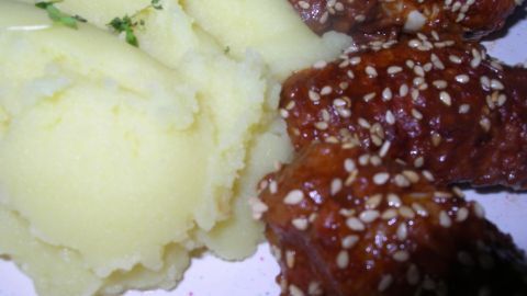 Auf einem Teller liegen zarte Hähnchenstücke in Schokoladensoße, umgeben von cremigem Kartoffelbrei.