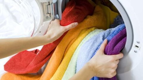 Bunte Handtücher werden aus einer Waschmaschine gezogen, während frische Wäsche vorbereitet wird, um muffigen Geruch zu vermeiden.