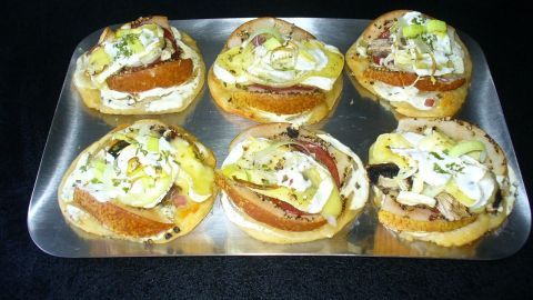 Sechs herbstlich belegte Aufbackbrötchen liegen auf einem Blech, garniert mit Fleisch und Gemüse in einer dunklen Umgebung.