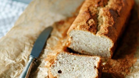 Ein Schnitten von frisch gebackenem Bananenbrot liegt auf braunem Papier, während ein Messer daneben liegt.