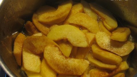 Zarte Apfelscheiben liegen in einem Topf mit einer Zuckermischung, bereit zum Kochen für die Quittentorte.