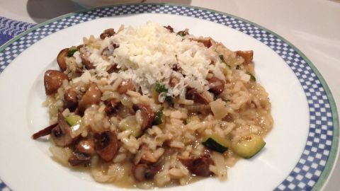 Ein cremiges Risotto mit Champignons und Zucchini liegt auf einem Teller, umgeben von einer eleganten blauen Serviette.