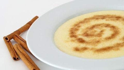 Ein Teller Grießbrei mit einer Zimtspirale darauf, daneben einige Zimtstangen auf weißem Hintergrund.