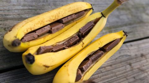 Gebackene Bananen liegen auf einem Holzbrett, gefüllt mit Schokoladenstückchen, bereit zum Backen.